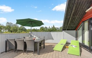 Un patio al aire libre con una mesa, sillas y dos sillones de descanso, además de un paraguas verde.