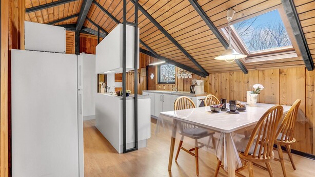 Una cocina moderna con vigas de madera, un comedor con mesa y sillas, y vista al exterior a través de un tragaluz.