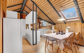Una cocina moderna con vigas de madera, un comedor con mesa y sillas, y vista al exterior a través de un tragaluz.