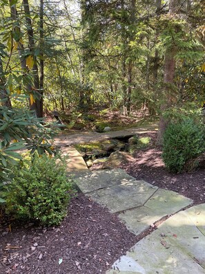 Ein bewaldetes Gebiet mit einer Steinbrücke, einem kleinen Bach und einem befestigten Weg.