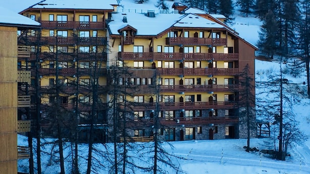 Un hotel a più piani con balconi, immerso tra alberi innevati e con le montagne sullo sfondo.