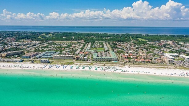 An aerial view of a coastal town with a beachfront, residential areas, and a large hotel complex.