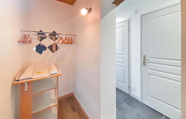 Un couloir avec une étagère en bois, un porte-manteau fixé au mur où sont suspendus des objets, et une porte blanche fermée.
