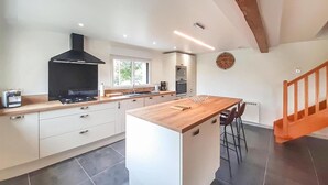 A modern kitchen with white cabinetry, a central island, a black range hood, and a clock on the wall. - Gorgeous home in Ledinghem with sauna (Ledinghem)