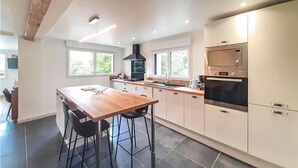 A modern kitchen with a wooden table, two bar stools, a black range hood, and stainless steel appliances. - Gorgeous home in Ledinghem with sauna (Ledinghem)