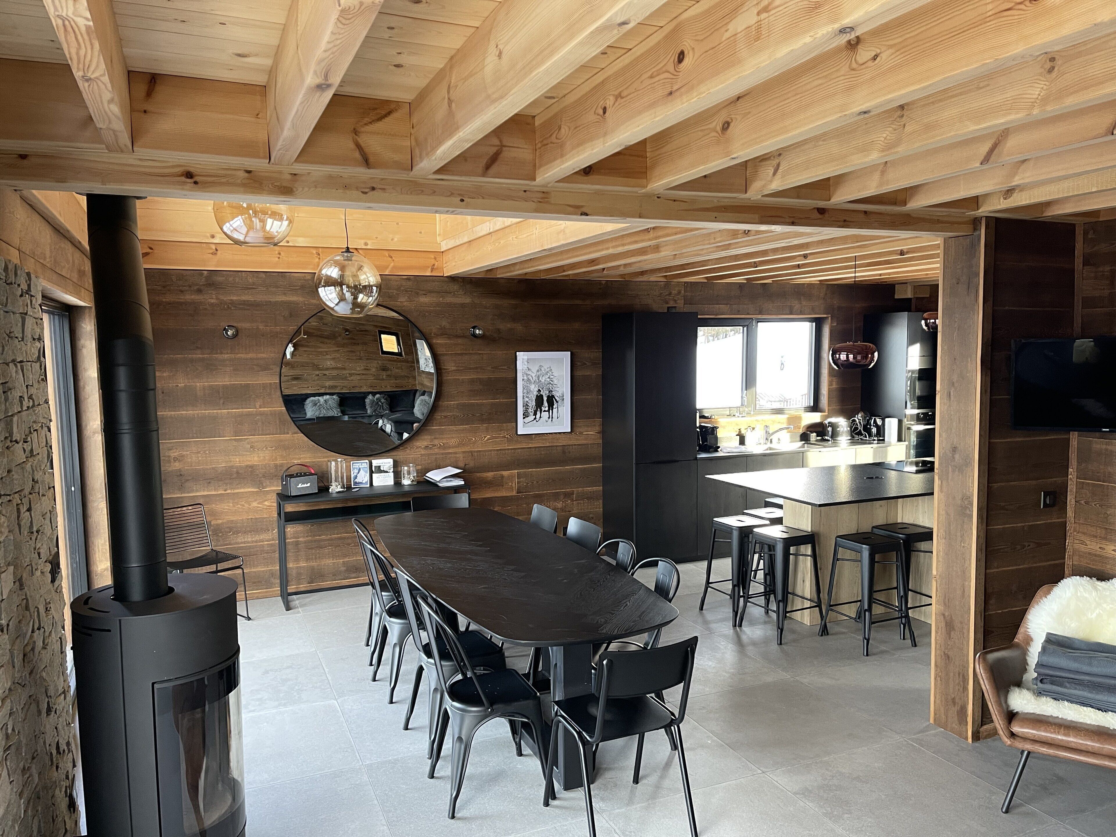 Une cuisine moderne dotée d’un grand îlot central, d’un coin repas avec une longue table et des chaises, et d’un plafond lambrissé.