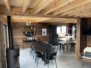 Una cocina moderna con una isla grande, una zona de comedor con una mesa larga y sillas, y un techo revestido de madera.