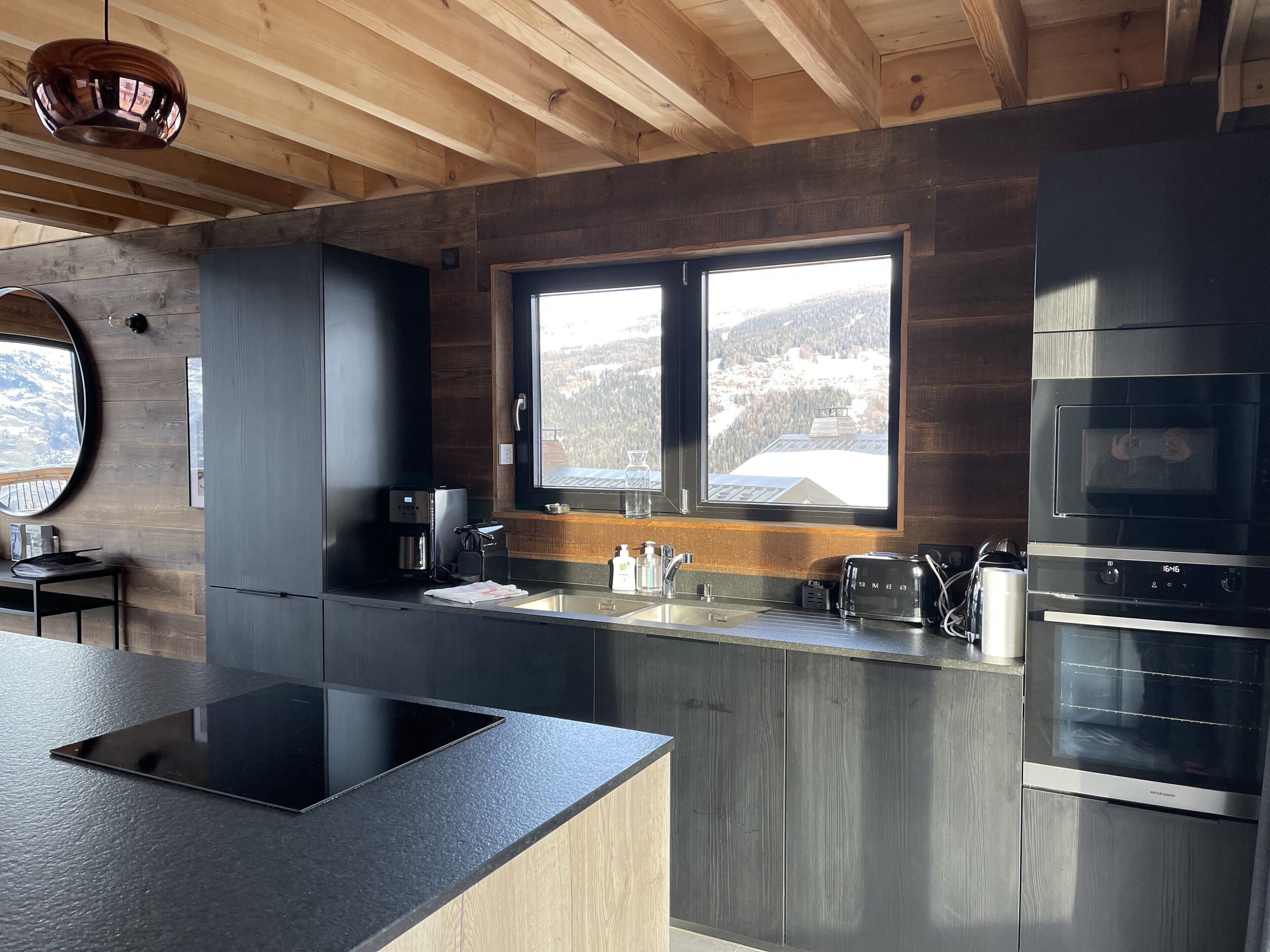 A modern kitchen with a large island, built-in appliances, and a window with a view of a snowy landscape.