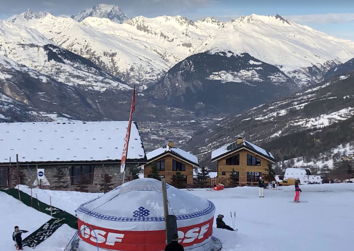 A snow-covered mountain landscape with a building that has a red and white sign, likely a hotel or lodge, with a view of the mountains in the background.
