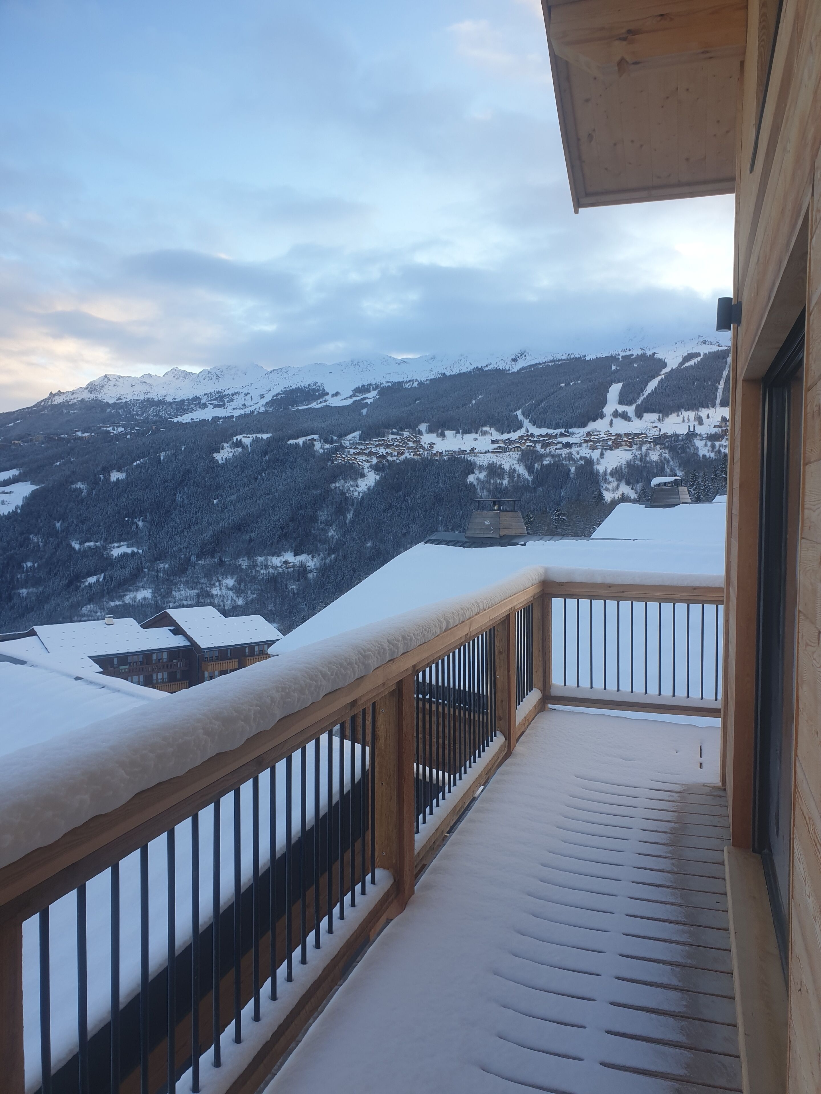 A wooden balcony with a metal railing overlooking a snow-covered mountain landscape.