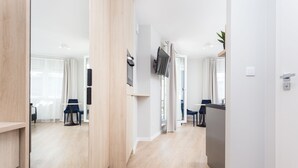 A modern hotel room with a wooden floor, a dining area with a table and chairs, and a TV mounted on the wall. - Studio with sunny terrace with Wawel Castle View - near Main Square  (Kraków)