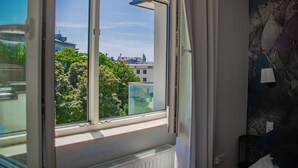 A room with a window overlooking a cityscape, a radiator, and a partial view of a bed. - Studio with sunny terrace with Wawel Castle View - near Main Square  (Kraków)