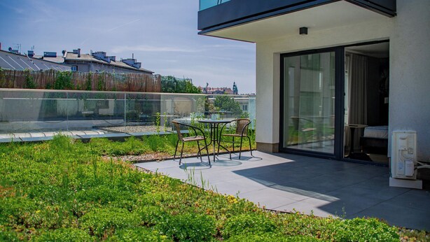 A modern outdoor patio with a glass balustrade, a table with chairs, and a view of the cityscape in the background. - Studio with sunny terrace with Wawel Castle View - near Main Square  (Kraków)
