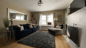 Un salon avec un canapé bleu foncé, un tapis gris, un plancher en bois, un ventilateur de plafond et une cheminée.