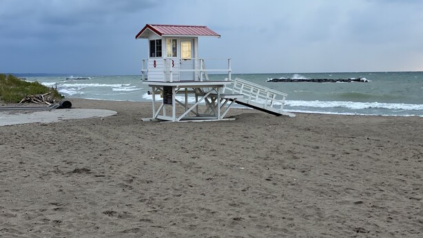 Une tour de surveillance, avec un toit rouge et des murs blancs, est située sur une plage de sable, avec l’océan en arrière-plan.