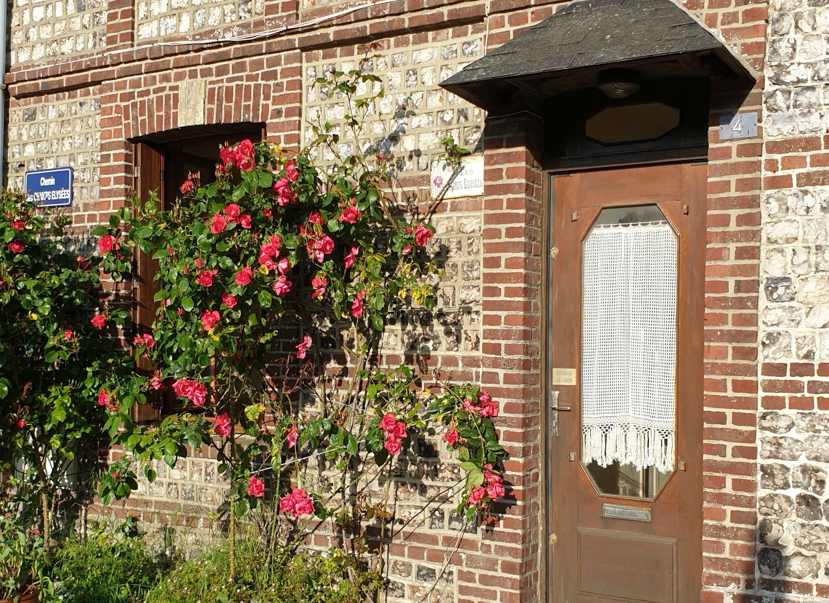 Un bâtiment en briques avec une porte en bois et une fenêtre. Il y a une enseigne au-dessus de la porte et une autre sur le mur.