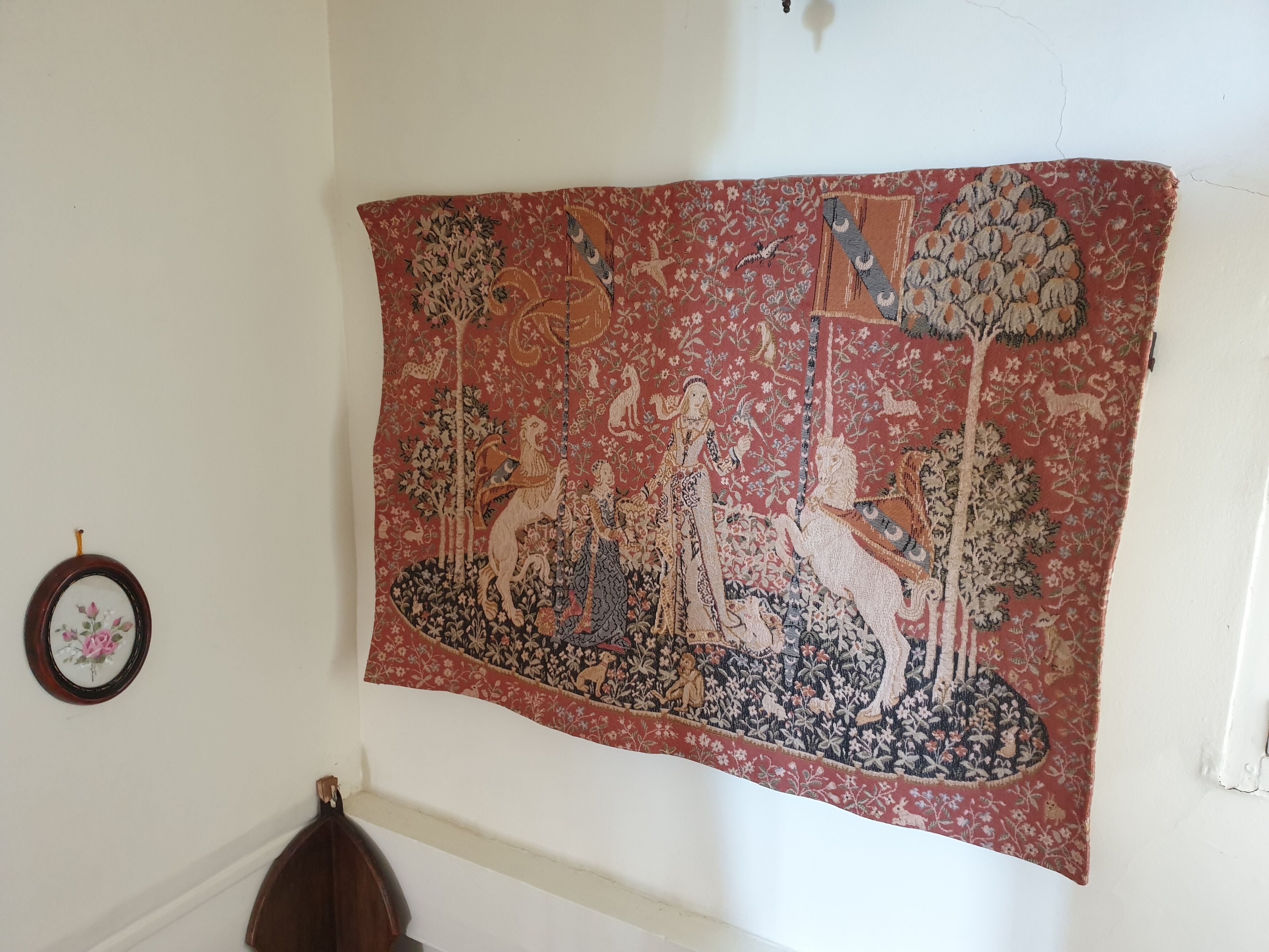 Une tapisserie représentant une figure centrale à cheval, entourée d’arbres et d’autres personnages, était accrochée à un mur blanc.