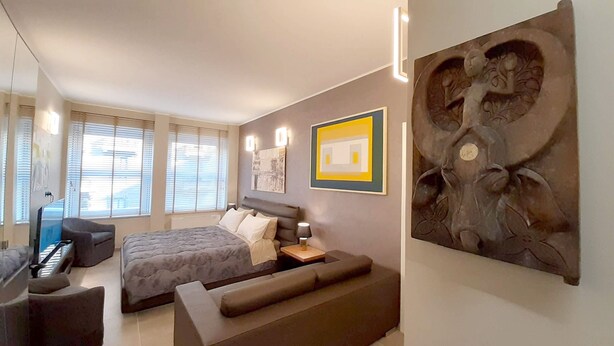 A modern bedroom with a bed, a sofa, a desk, and a large abstract painting. - Suite Central Station Milano (Milano)