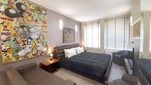 A bedroom with a large bed, a small sofa, a desk, and a window with blinds. - Suite Central Station Milano (Milano)