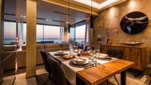 Ein moderner Essbereich mit Holztisch, gedeckt für eine Mahlzeit, große Fenster mit Blick und einer runden Wanduhr.