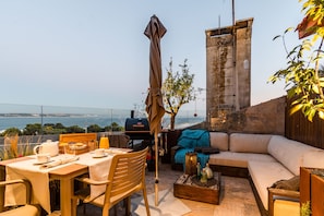 Enjoy al fresco dining with a view of the sea from this outdoor seating area, featuring a dining table, sofa, and barbecue grill.