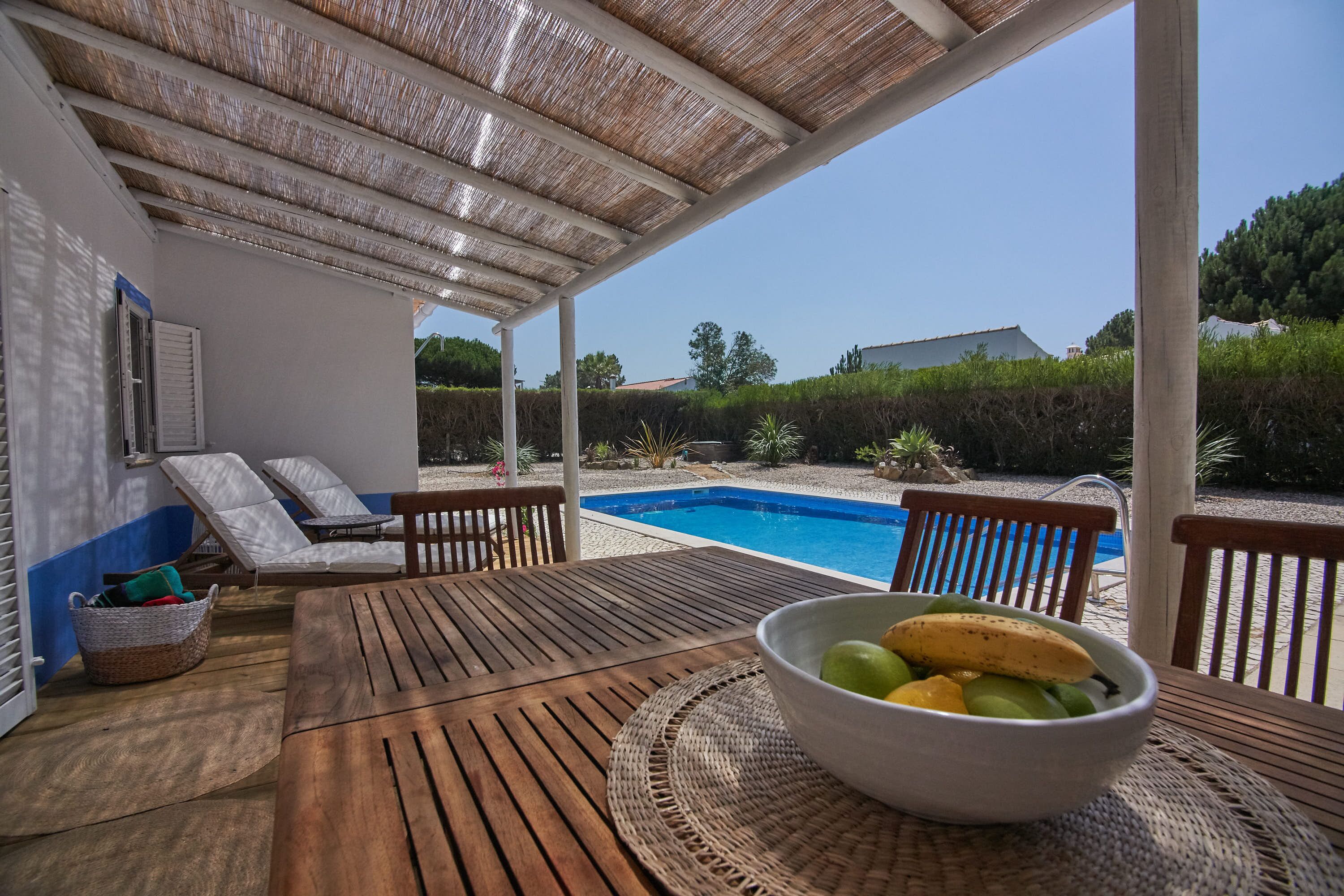 Zona exterior coberta amb piscina, gandules i taula amb un bol de fruita.