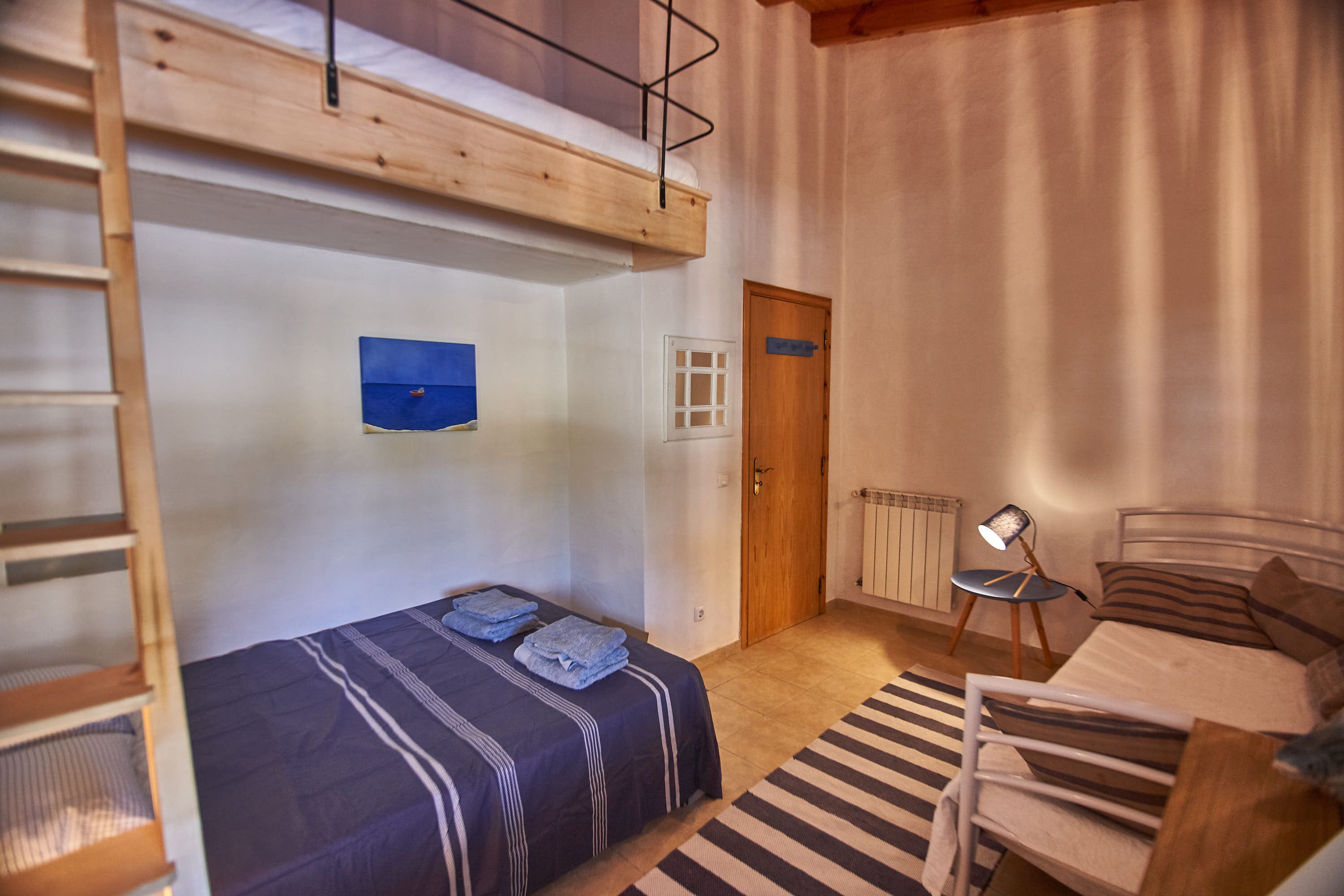 Une chambre avec un lit superposé, une petite table avec une lampe, un radiateur et une porte.