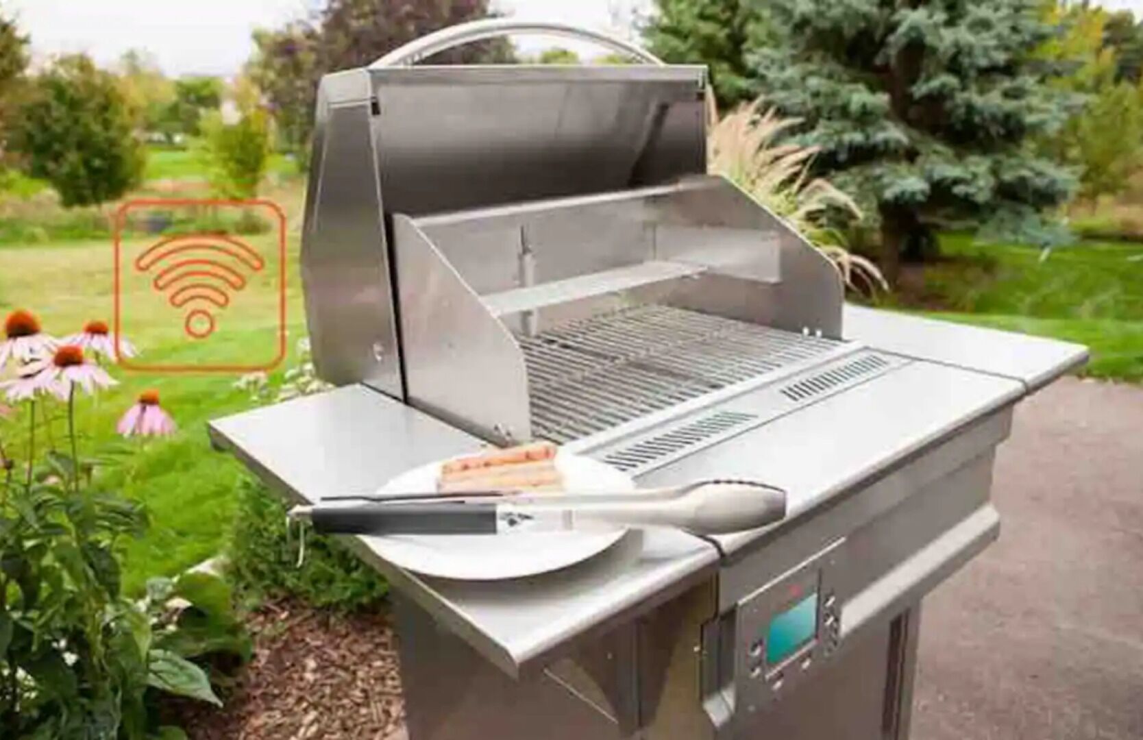A portable grill with a digital display, a spatula, and a plate, set in a garden with flowers and trees.