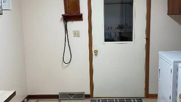 Una stanza con pavimento piastrellato, una porta con finestra, un piccolo armadietto in legno, un termosifone e un elettrodomestico bianco.