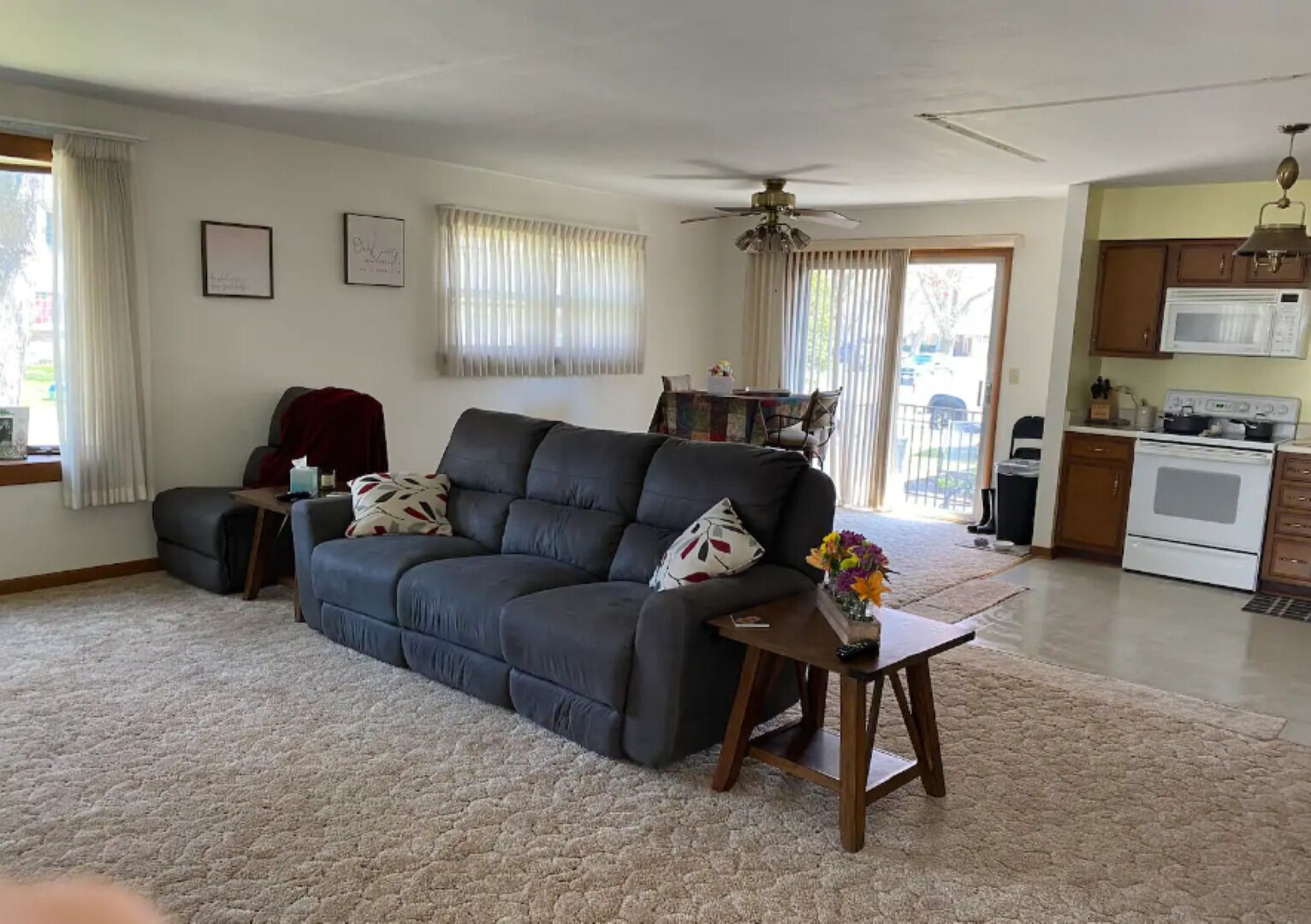 A living room with a dark grey sofa, a wooden coffee table, and a kitchen area with a microwave and stove.