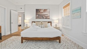 Quarto com cama de madeira, roupa de cama branca e tapete estampado.