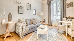 A living room with a sofa, coffee table, and dining table. There are framed pictures on the wall, a vase, and a lamp. - Andromeda Luxury Apartment in Colosseum (Roma)