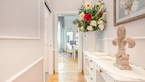 A hallway with a white console table, a vase of flowers, and a framed floral painting on the wall. - Andromeda Luxury Apartment in Colosseum (Roma)