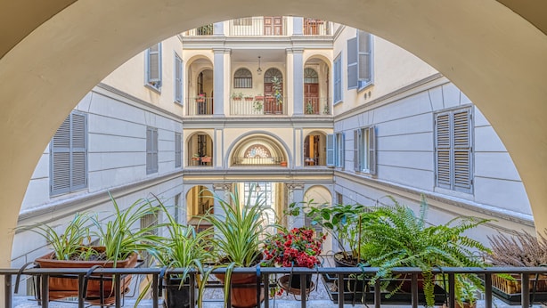 A courtyard with a central balcony, potted plants, and a view of a building with multiple windows and balconies. - Andromeda Luxury Apartment in Colosseum (Roma)