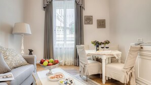 A cozy living room with a sofa, a dining table with chairs, a lamp, and a window with curtains. - Andromeda Luxury Apartment in Colosseum (Roma)
