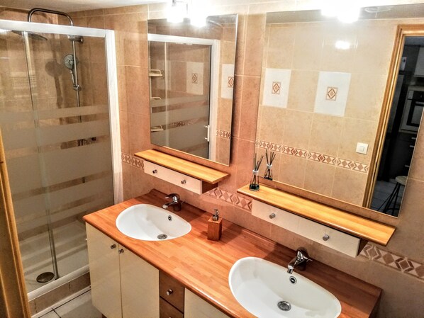 Baño con dos lavamanos, ducha y un espejo grande.