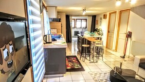Cocina compacta con refrigerador, cafetera y un pequeño comedor con taburetes.