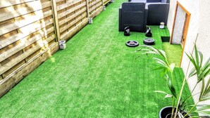 Un pequeño espacio al aire libre con césped artificial verde, valla de madera y equipamiento de ejercicio.