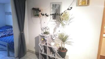 A room with a bed, a plant shelf, and a small table with a lamp.