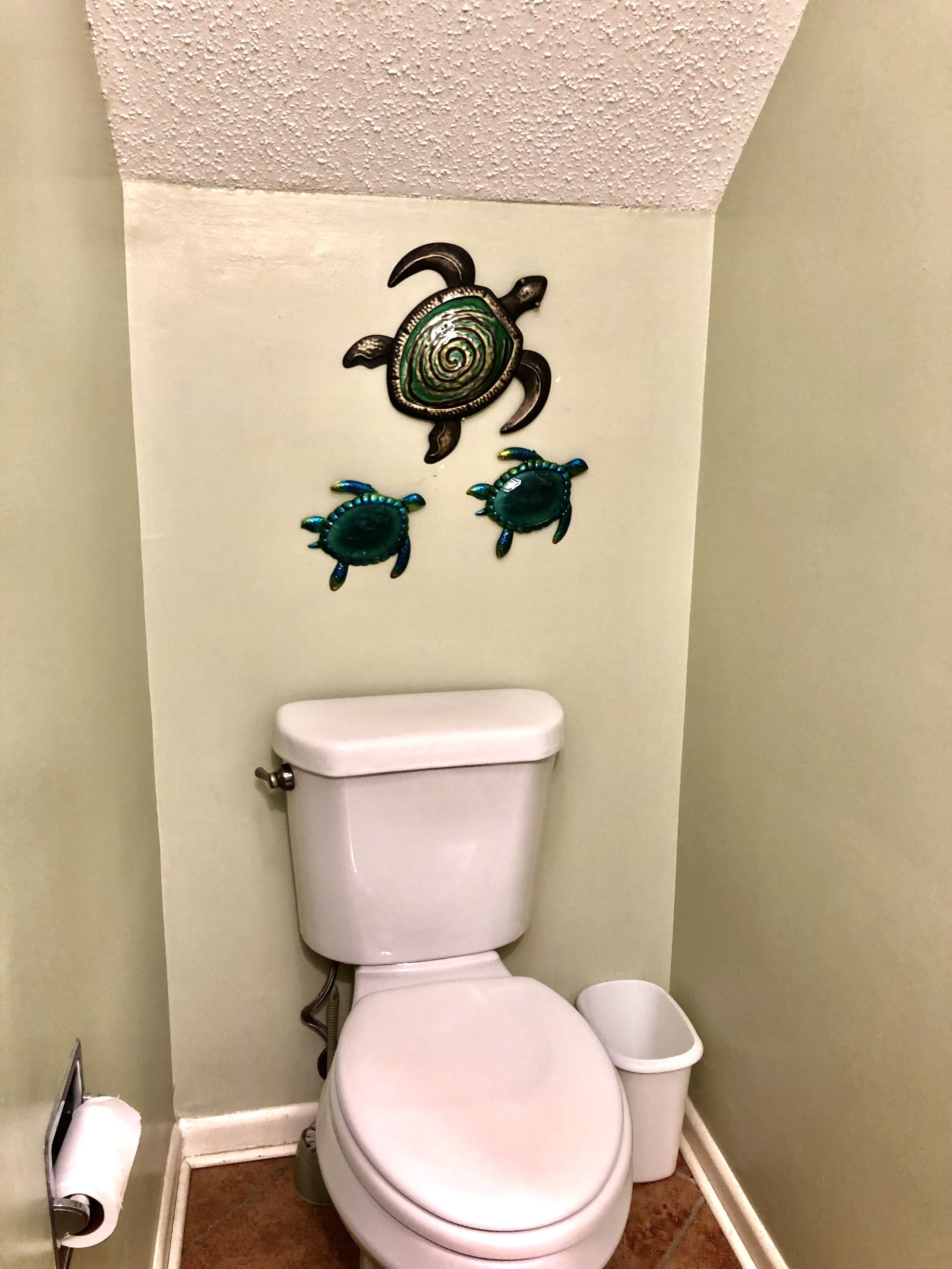 A bathroom with a toilet, a trash bin, and decorative turtle wall art.