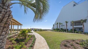 A modern building with a covered outdoor area, a paved pathway, and palm trees. - Destin, FL Spacious 3BR Condo,  Family Friendly  (Destin)