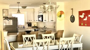 A modern kitchen with white cabinetry, a dining table with chairs, a chandelier, and a wall-mounted mirror. - Destin, FL Spacious 3BR Condo,  Family Friendly  (Destin)