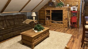 L’intérieur chaleureux d’un chalet en bois comprend une chambre à coucher située en mezzanine, des meubles en bois, un téléviseur et une cheminée.
