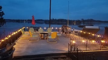 Relax in a serene outdoor seating area with comfortable chairs and tables, surrounded by a low fence and offering a waterfront view.