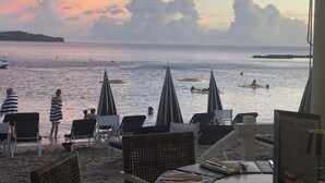 Une vue sur la plage, avec des chaises longues et des parasols, une mer calme et un ciel au coucher du soleil.