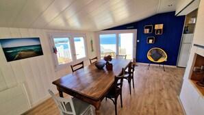 A dining area with a wooden table and chairs, a view of the sea through large windows, and a blue accent wall. - Villa Ti Ann 4 persons, sea view. stand 50 meters (Cleder)