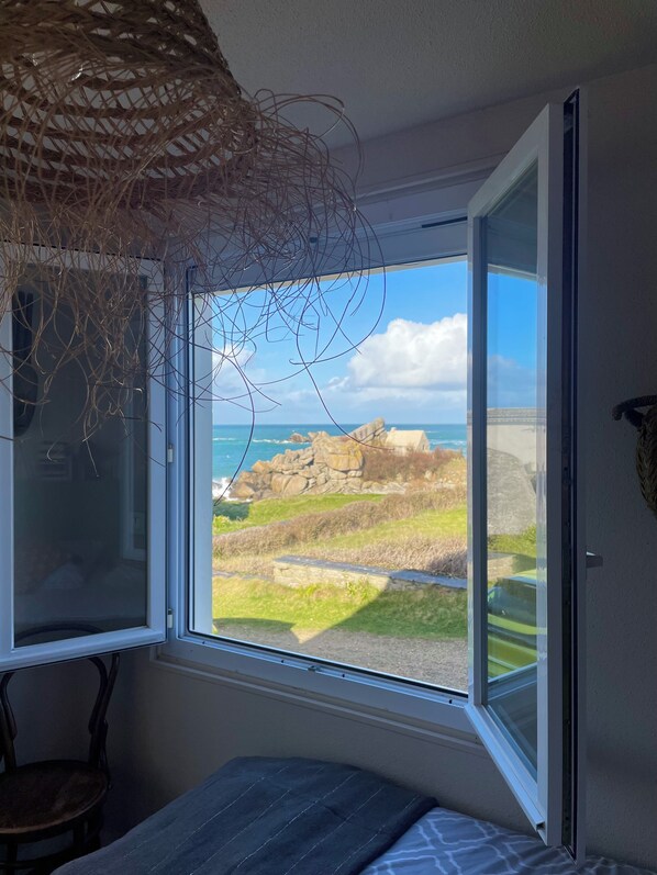 A room with a large window offering a view of rocky terrain and a beach. - Villa Ti Ann 4 persons, sea view. stand 50 meters (Cleder)