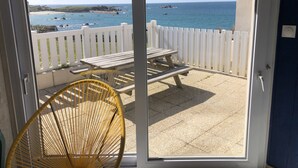 A balcony with a white fence, a wooden table, and a wicker chair. - Villa Ti Ann 4 persons, sea view. stand 50 meters (Cleder)