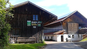 A rustic wooden building with a bench outside, a bicycle, and a signboard. - Ihr Ferienhof am Rande der Alpen (Seeg)