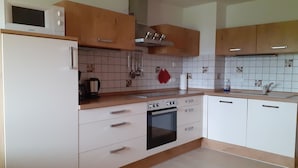A kitchen with white cabinets, a microwave, a stove, and a sink. - Ihr Ferienhof am Rande der Alpen (Seeg)